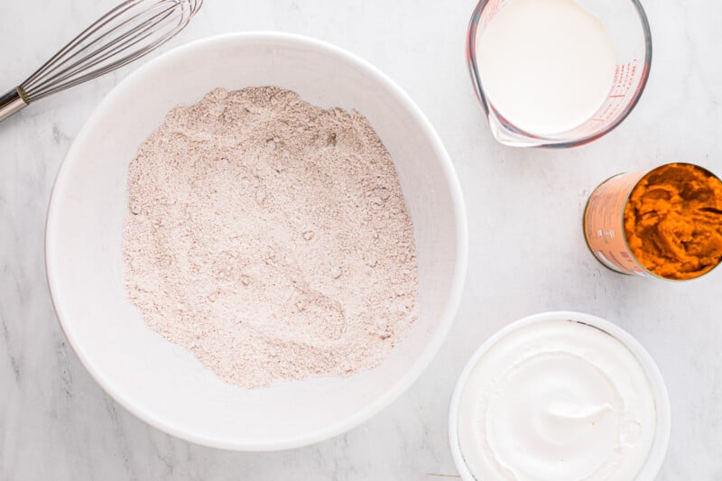 A white bowl with ingredients and a whisk.