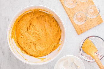 A bowl of pumpkin icing with a spoon and a glass.