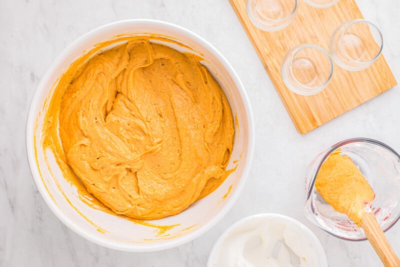 A bowl of pumpkin icing with a spoon and a glass.