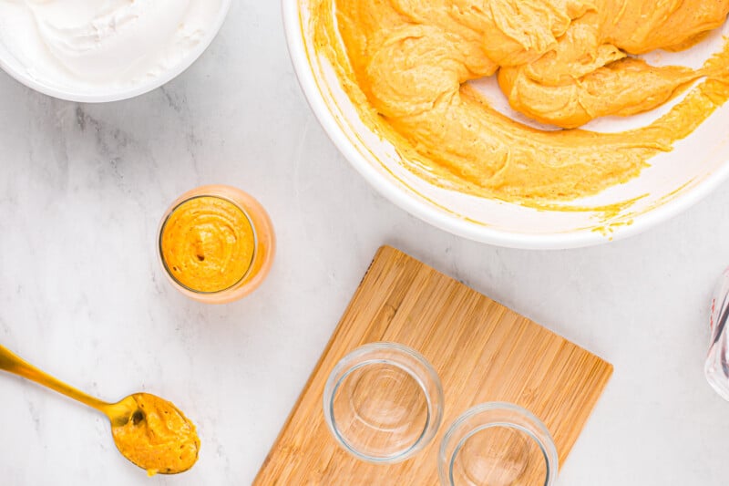 A wooden cutting board with a bowl of icing and a spoon.