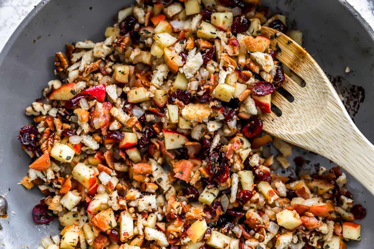 Cranberries and apples in a pan with a wooden spoon.