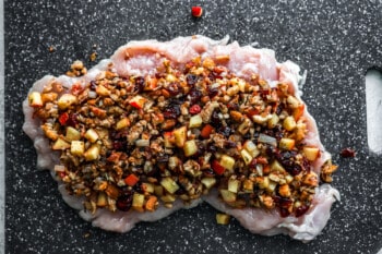 A piece of chicken with nuts and raisins on a cutting board.