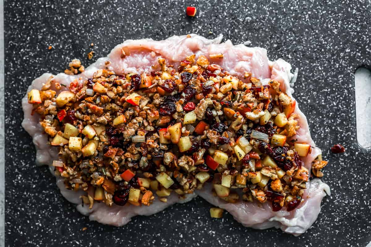 A piece of chicken with nuts and raisins on a cutting board.