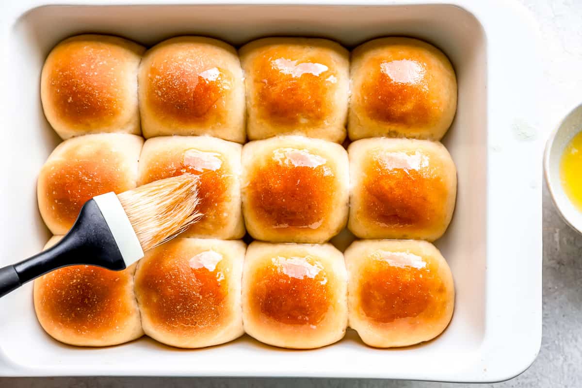 Rolls in a baking dish with a brush.