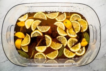 A glass bowl filled with lemon slices and sprigs of sage.