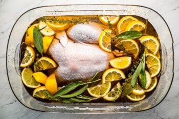 A chicken in a glass bowl with lemons and sprigs of thyme.