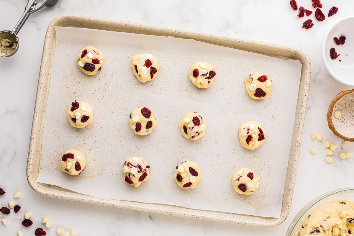 cookie dough balls with cranberries and white chocolate chips on a baking sheet.