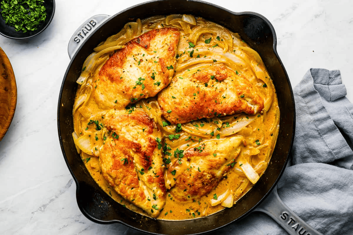 chicken breasts cooking in a pan with gravy