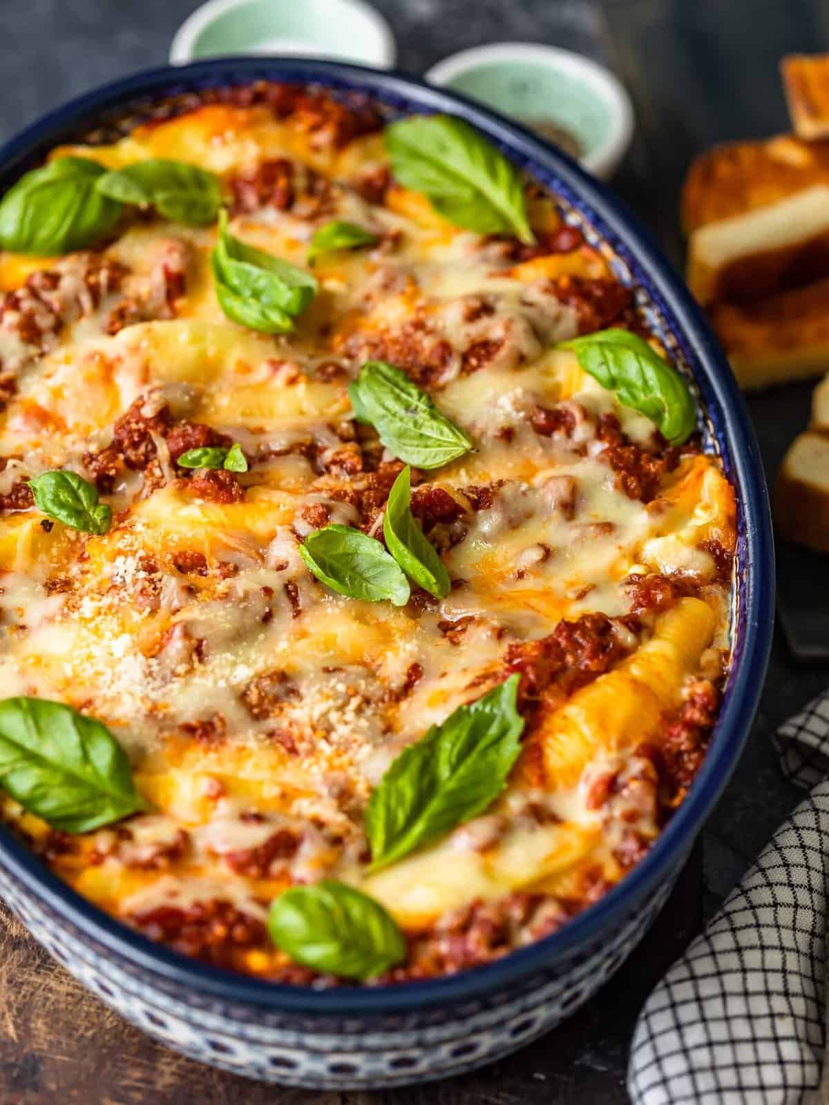 stuffed pasta shells in a blue casserole baking dish topped with melted cheese and fresh basil