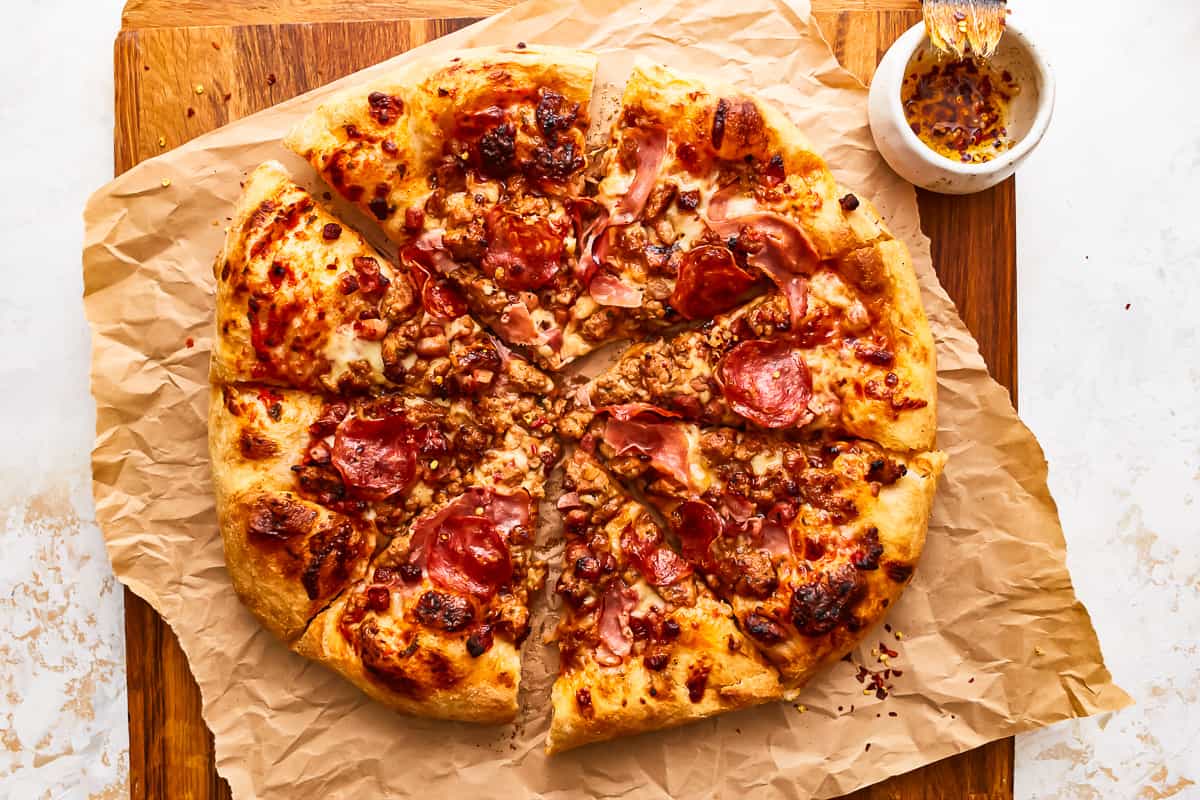 A sliced meat lovers pizza on parchment on a wooden cutting board.