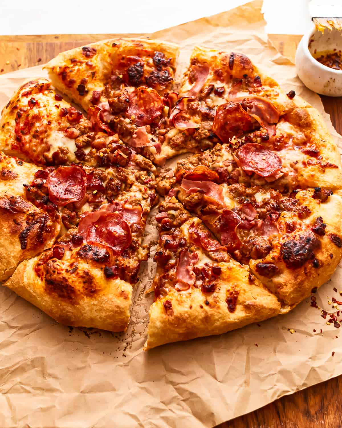 A sliced meat lovers pizza on parchment paper.