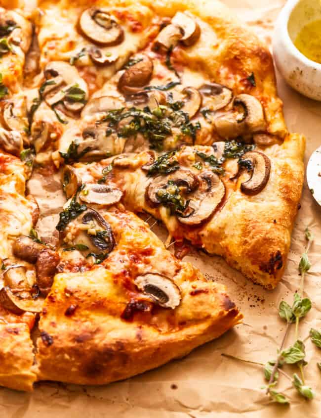 A pizza with mushrooms and herbs on a piece of paper.
