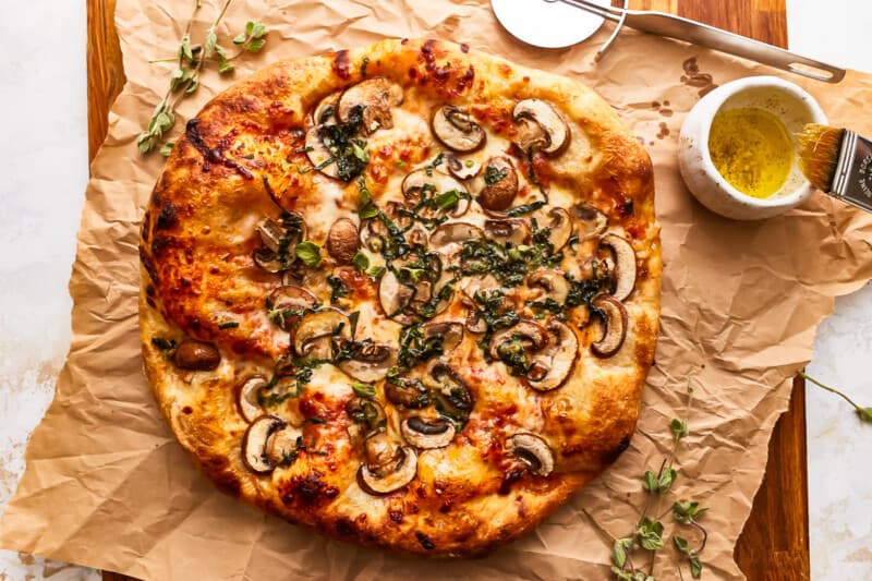A pizza with mushrooms and herbs on top of a piece of brown paper.