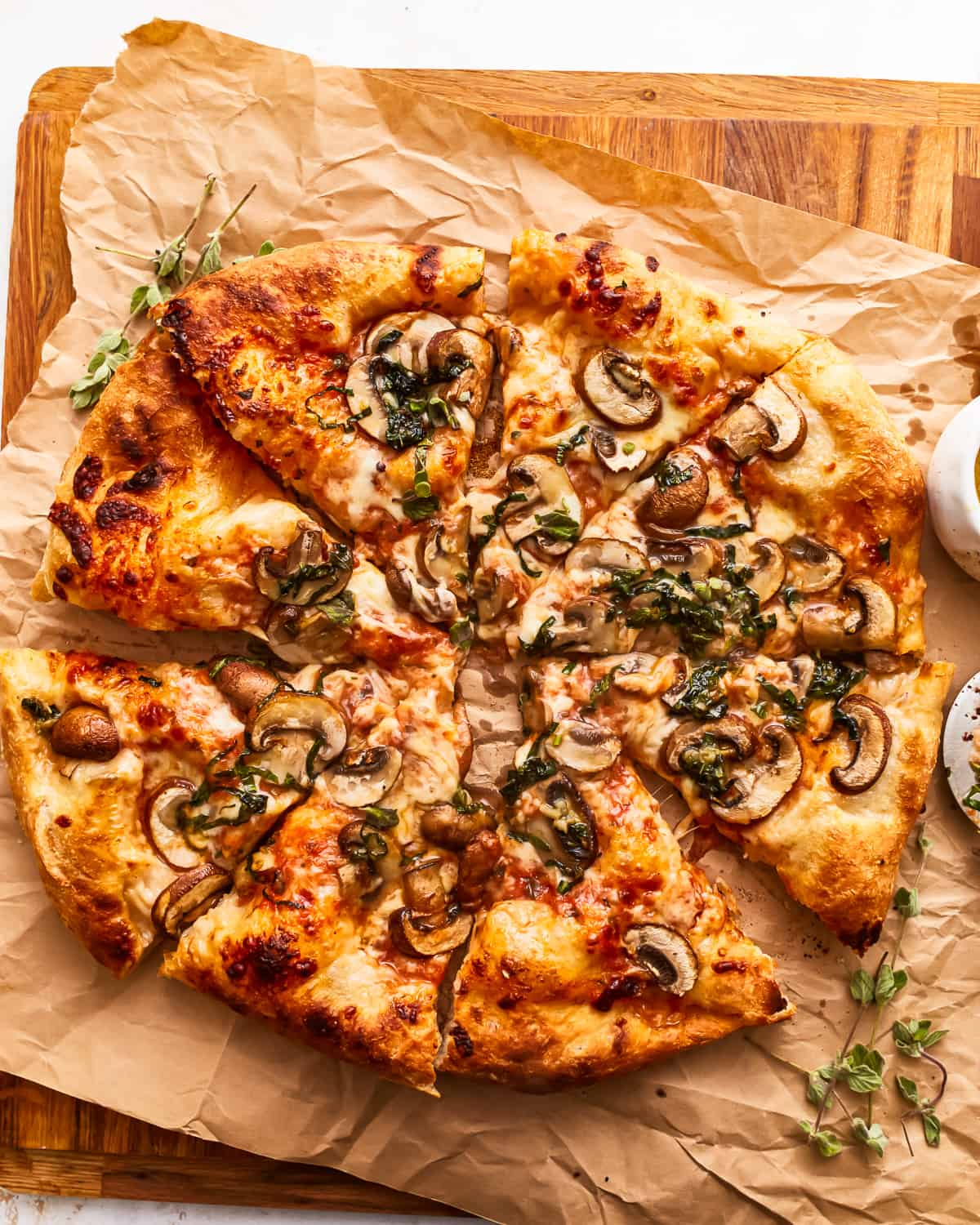 A pizza with mushrooms and herbs on a wooden cutting board.