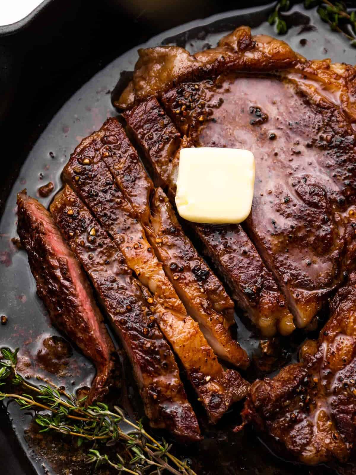 close up of partially sliced oven baked steak with a pat of butter on top in a cast iron pan.