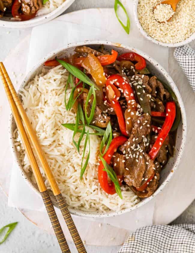 a bowl of beef and pepper stir fry with rice and chopsticks.