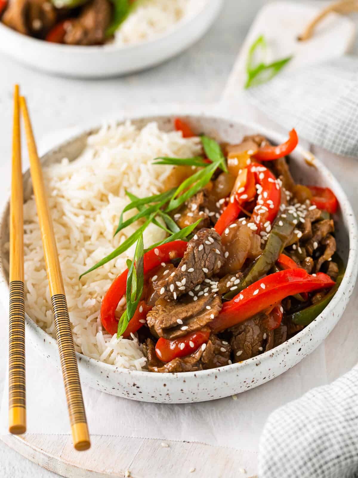 a bowl of stir fry with beef, peppers, onions, and white rice.