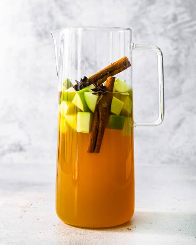 A pitcher of apple cider with cinnamon sticks in it.