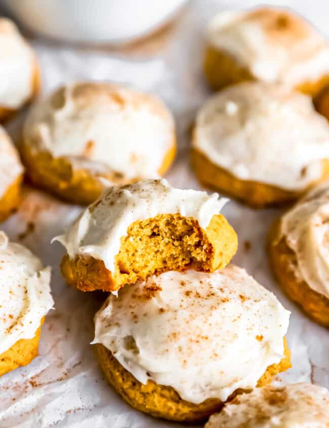 Pumpkin cookies with icing and a bite taken out.