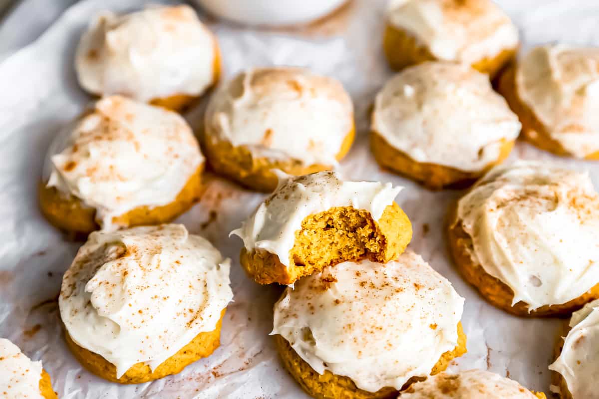 Soft pumpkin cookies with icing and cinnamon on a baking sheet.