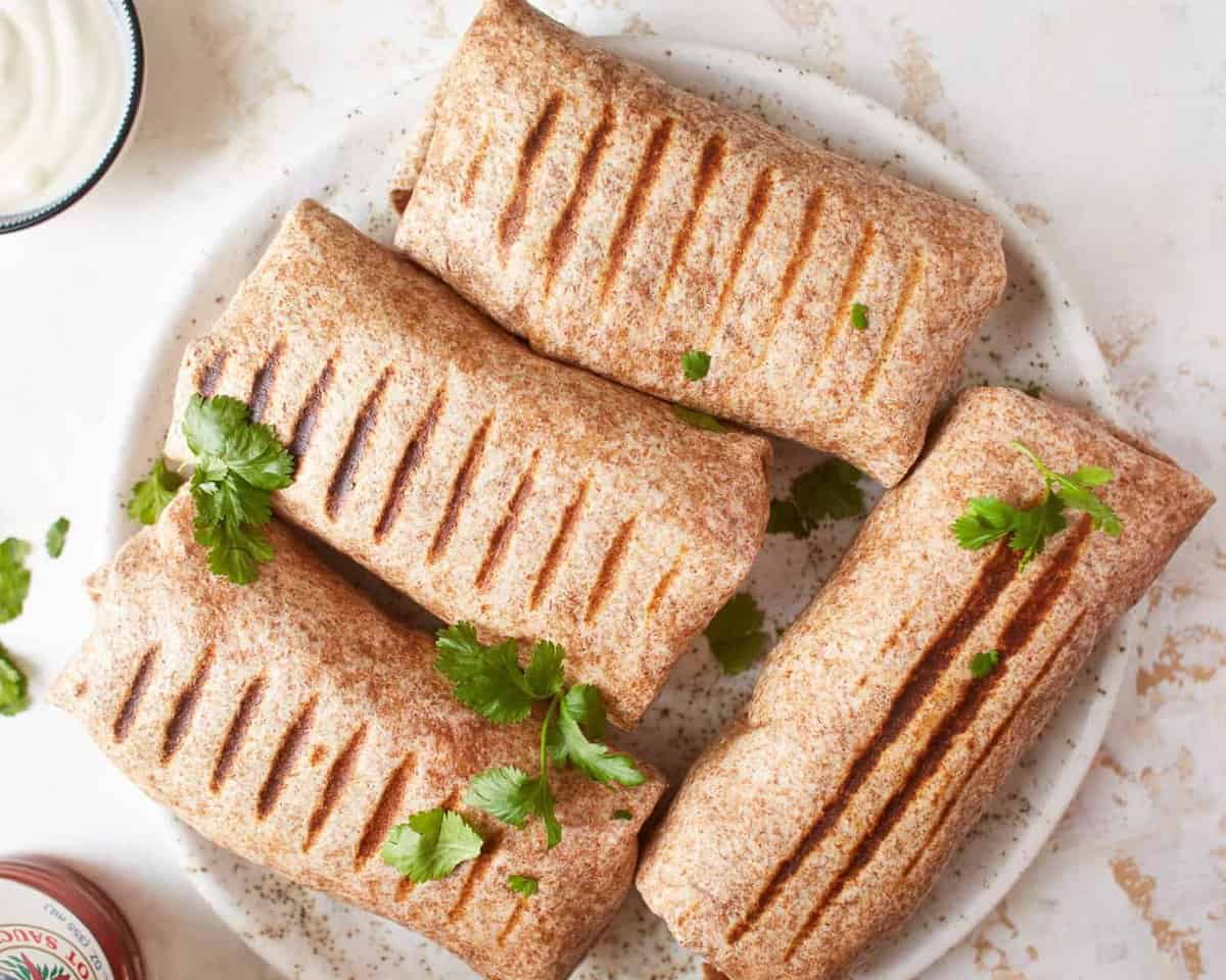 overhead view of 4 grilled chicken ranch wraps on a white plate.