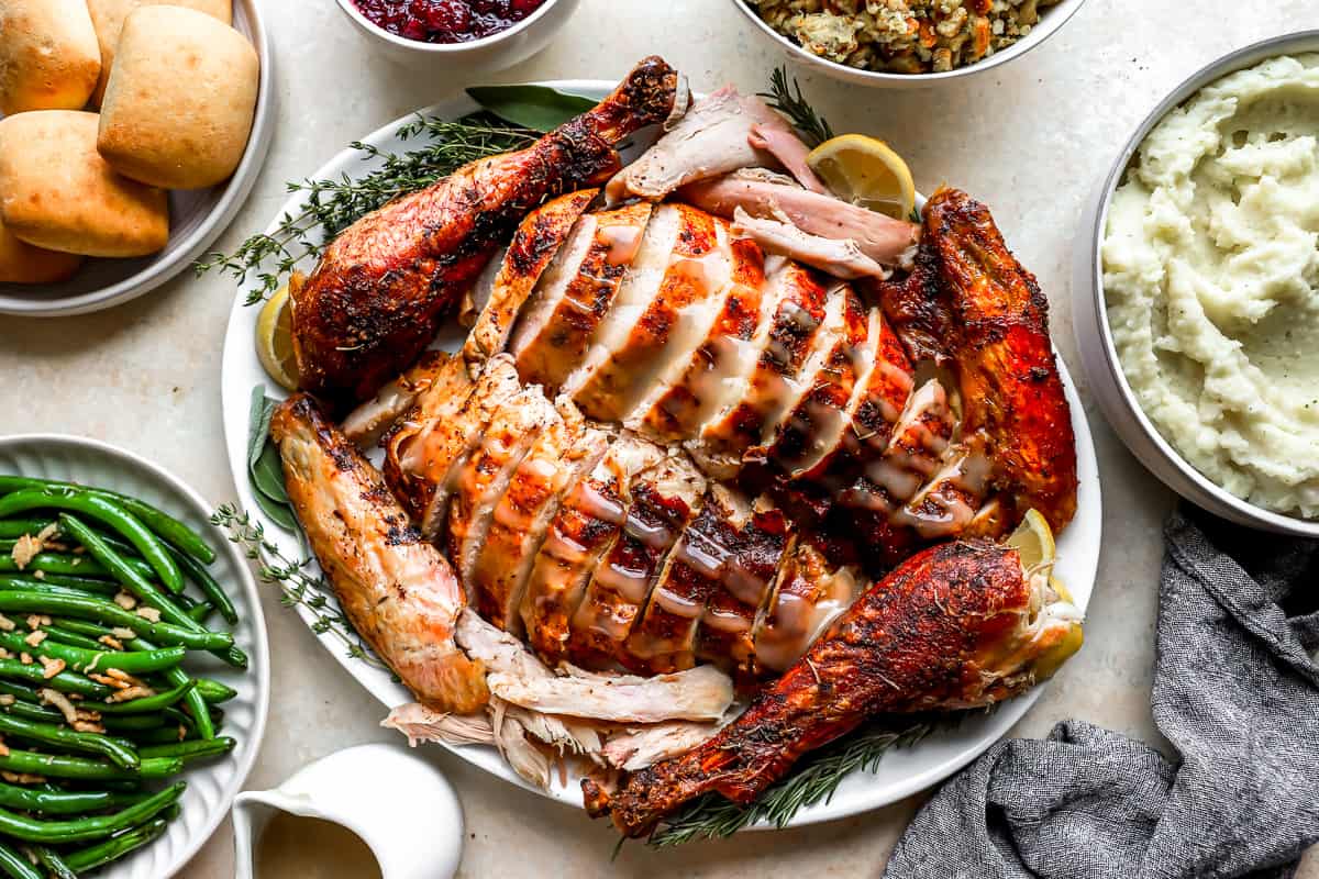 Carved turkey on a serving dish surrounded by Thanksgiving sides.