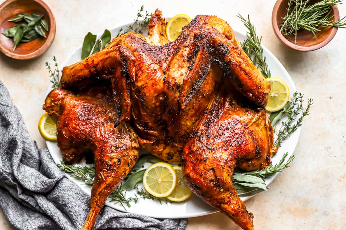 A spatchcocked turkey on a plate with lemons and herbs.