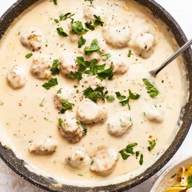 A bowl of pasta with meatballs and parsley.