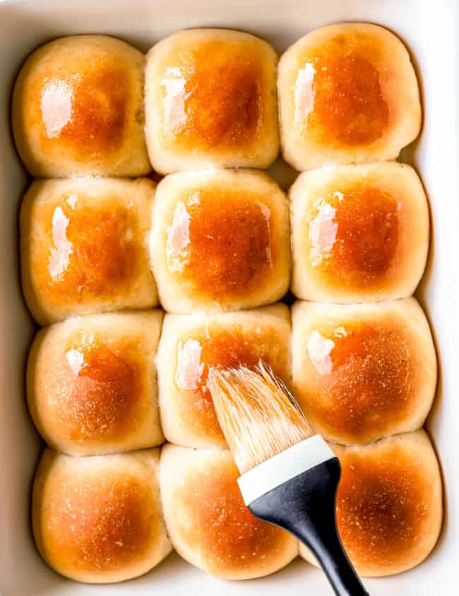 A baking dish filled with buns and a brush.