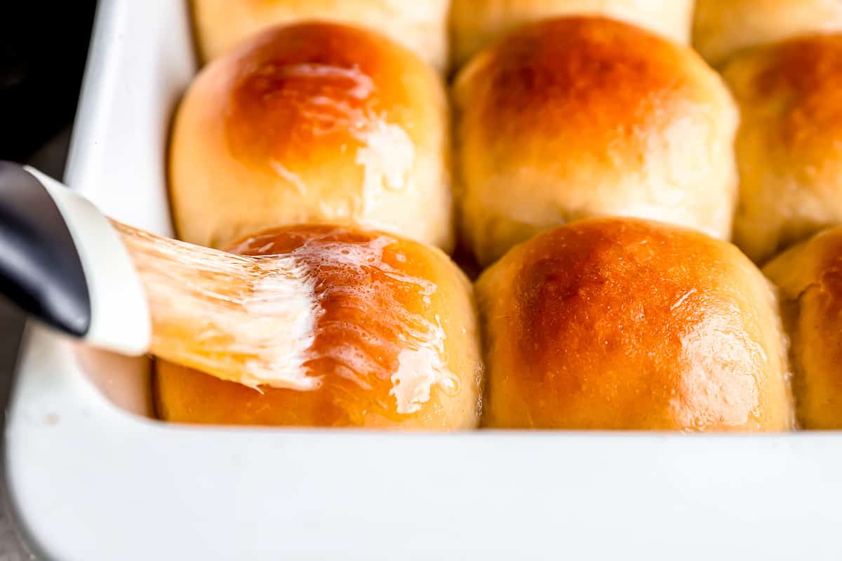 A person is using a spatula to spread butter on bread rolls.