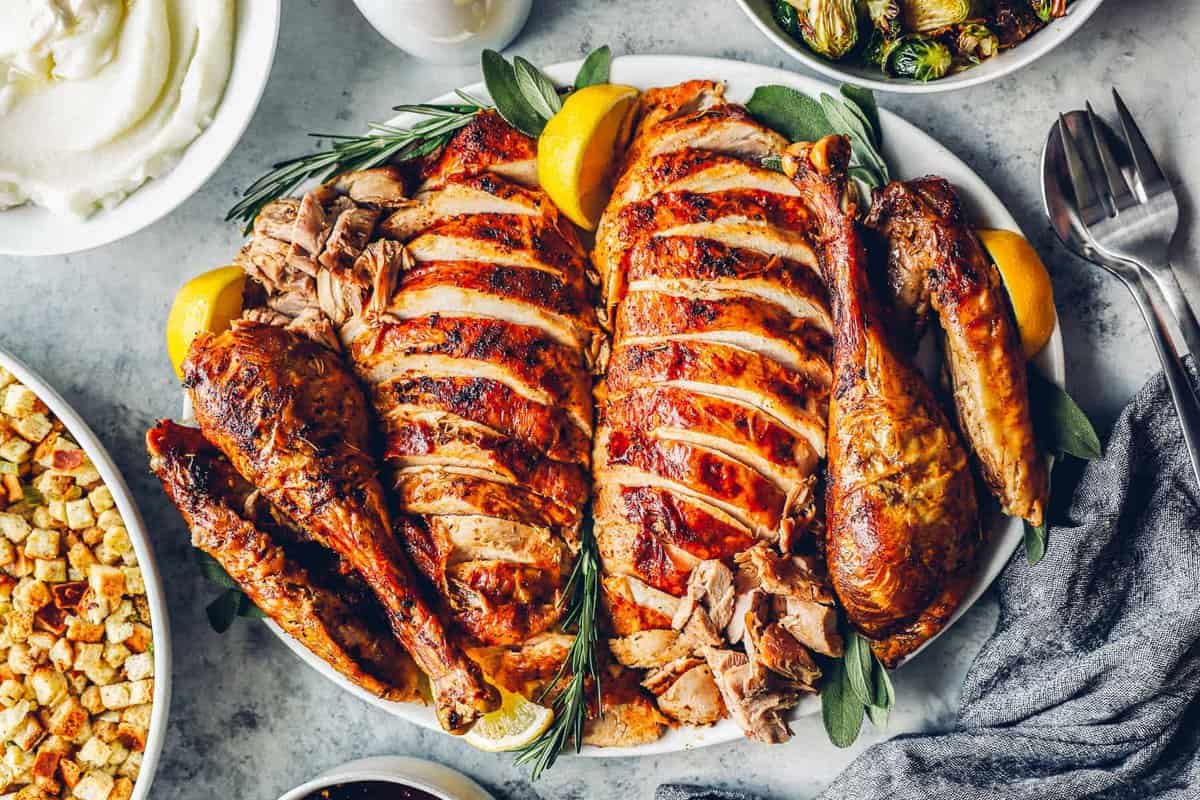 carved and sliced roast turkey on a serving platter, at the center of a Thanksgiving dinner table.