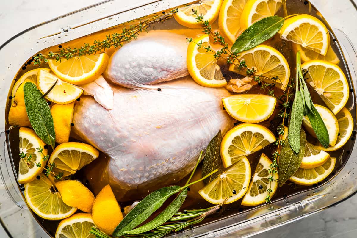 A turkey brining in a glass container with lemons and sprigs of thyme.