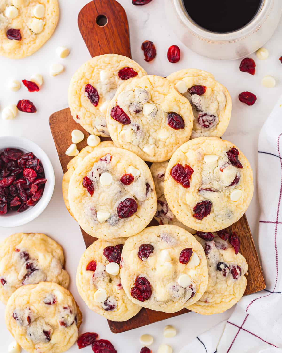 White chocolate cranberry cookies piled on a wooden cutting board.