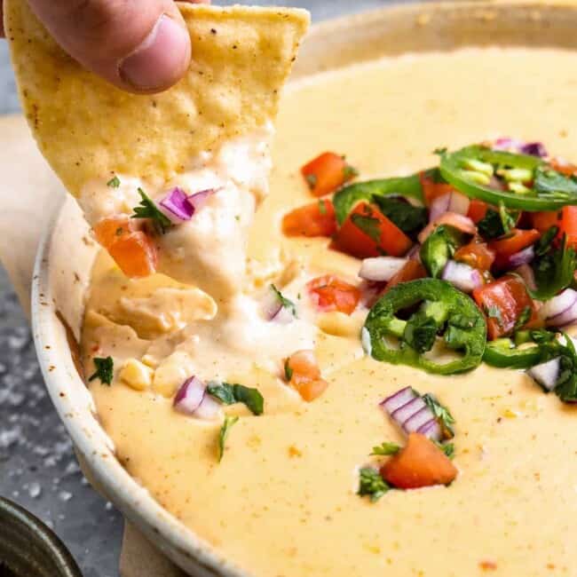 a person dipping a tortilla into a bowl of mexican dip.