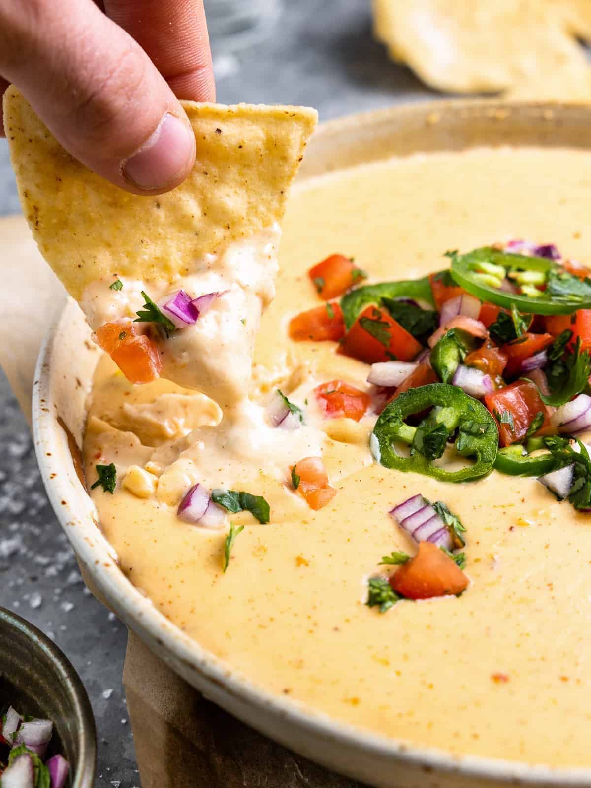 a hand dopping a tortilla chips into a bowl of homemade queso blanco.