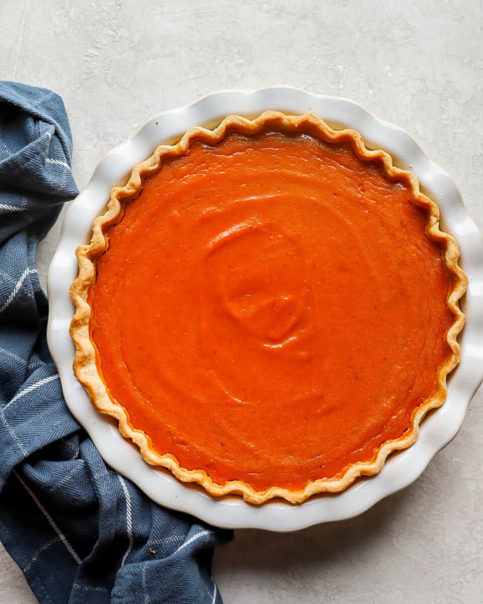 A pumpkin pie on a white plate with a blue cloth.