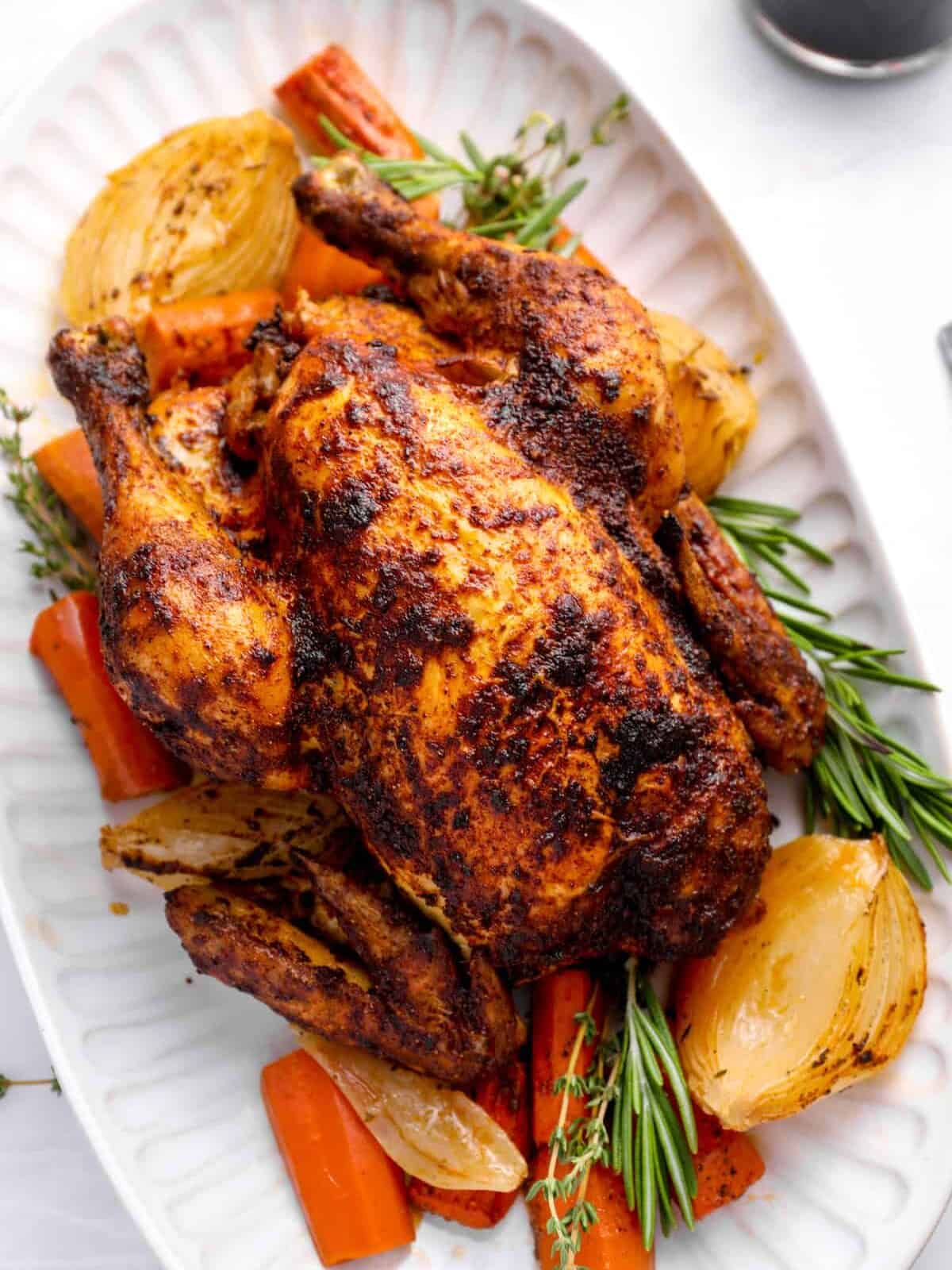 crockpot whole chicken on a white serving platter with vegetables and herbs.