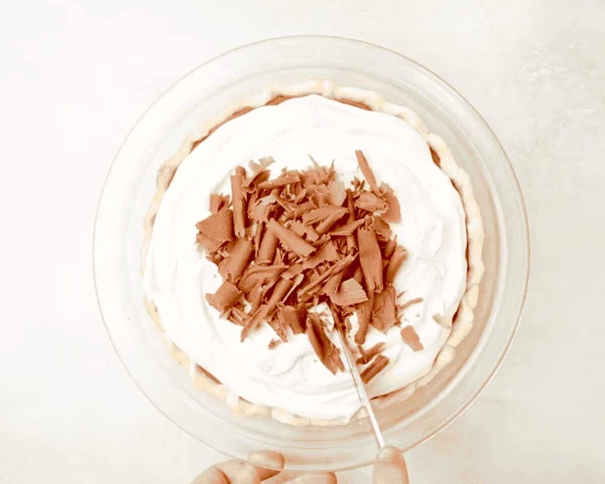 French silk pie topped with whipped cream and chocolate shavings being cut into. 
