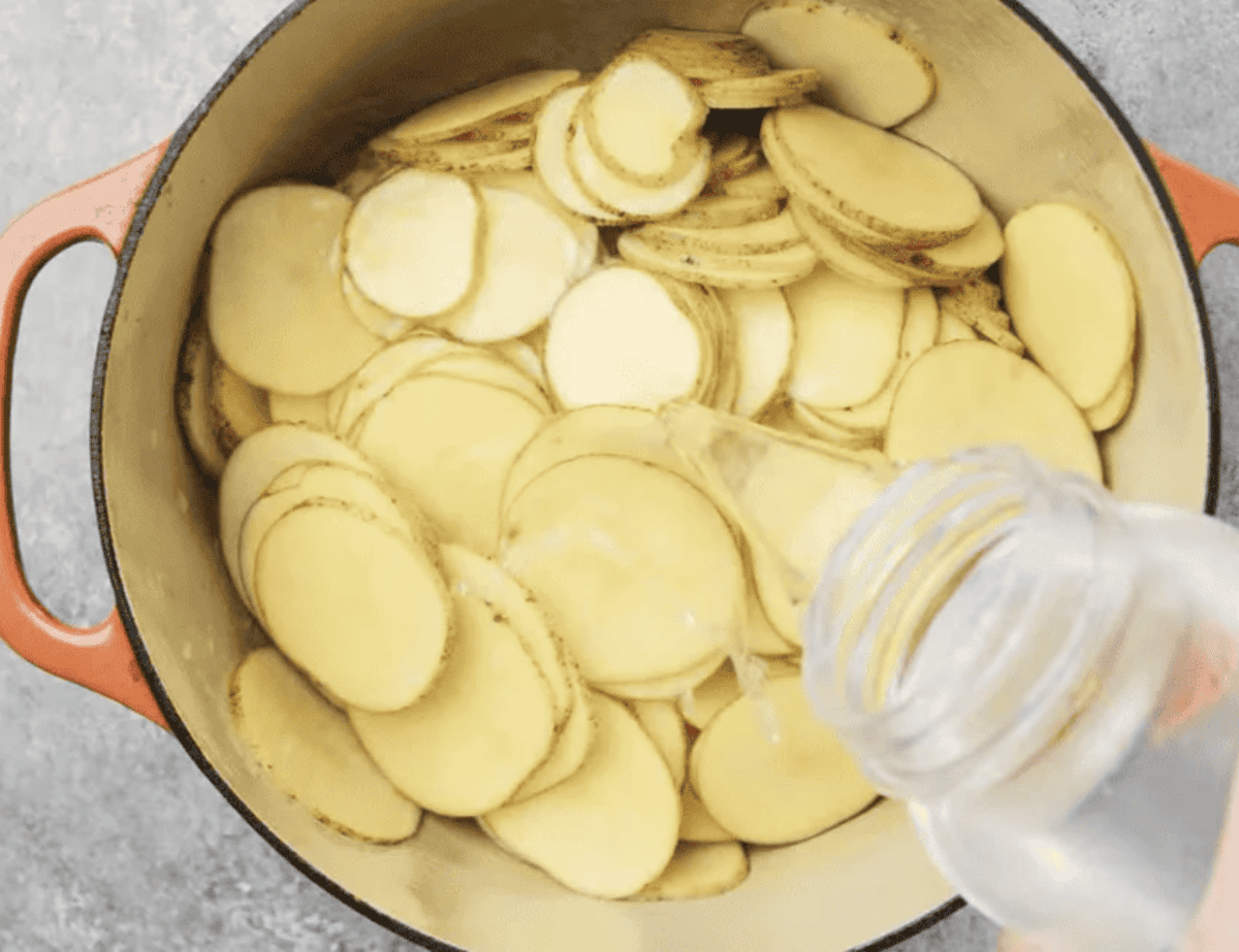 Pouring water over sliced potatoes in a pot.