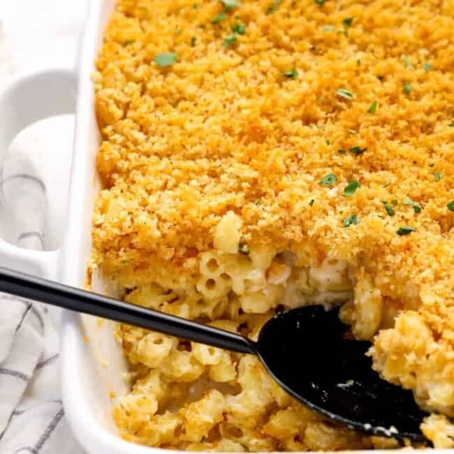 close up of mac and cheese casserole in a white baking pan with a black serving spoon.