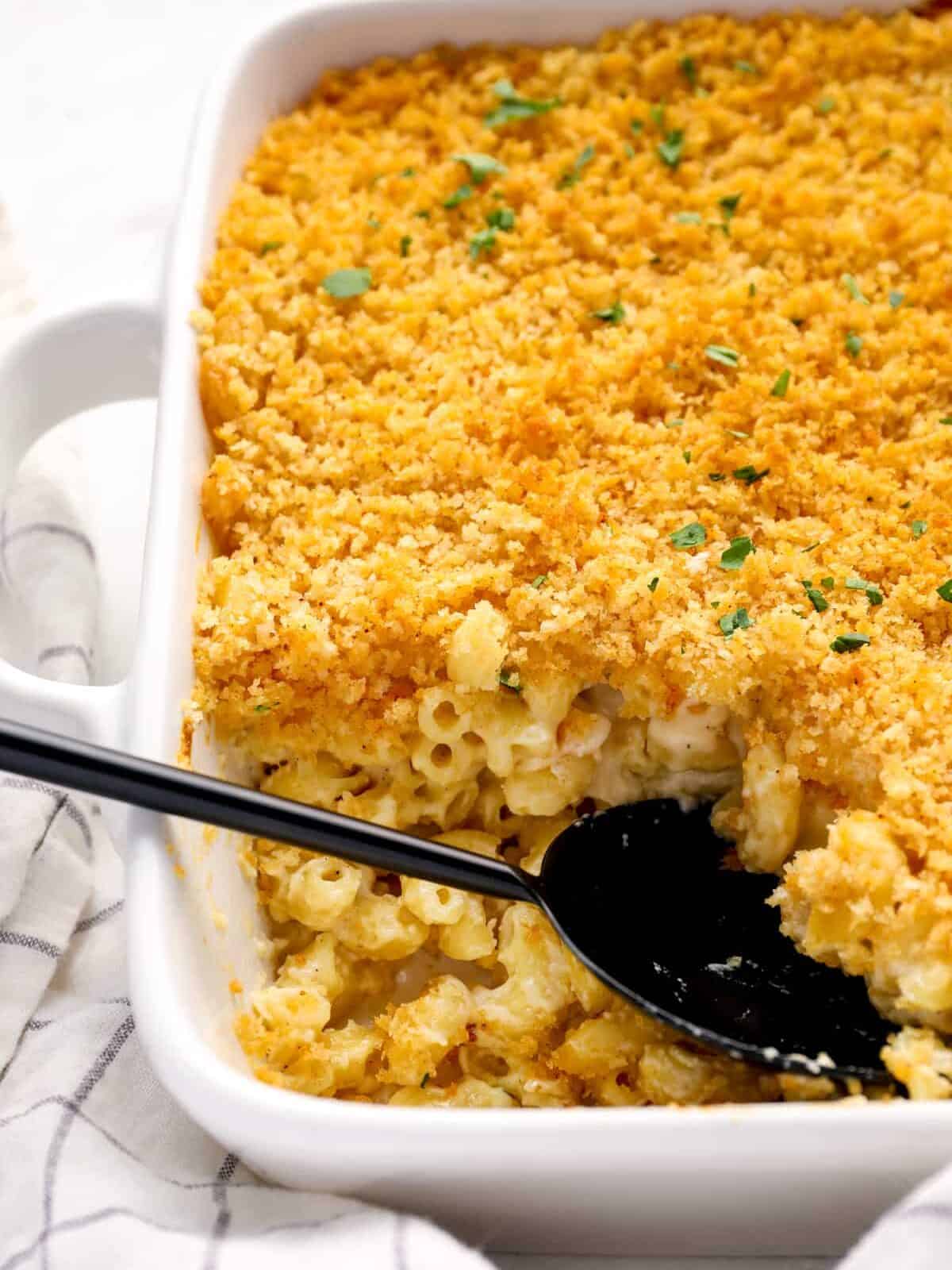 close up of mac and cheese casserole in a white baking pan with a black serving spoon.