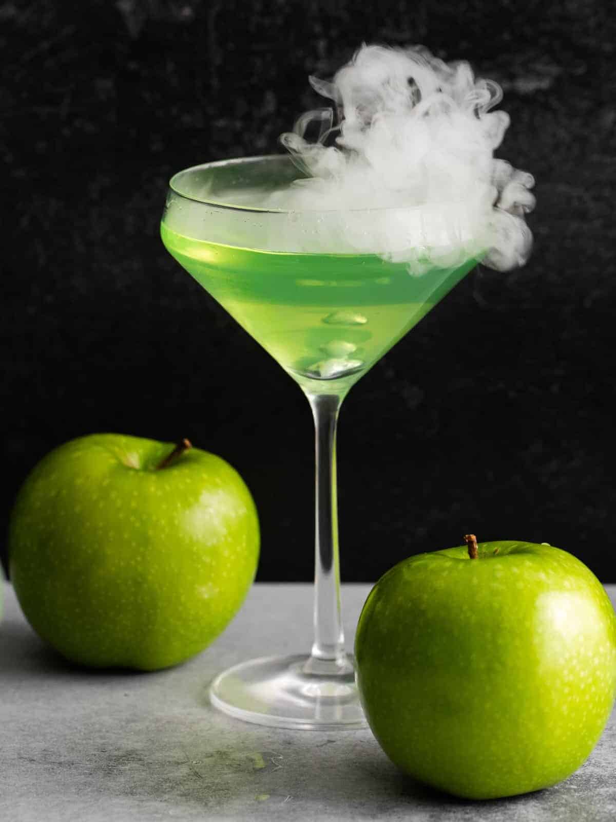 close up of a green poison apple martini with 2 green apples.