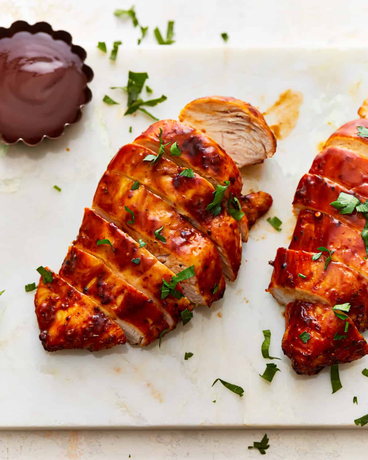 Two Air Fryer BBQ chicken breasts on a cutting board with sauce.