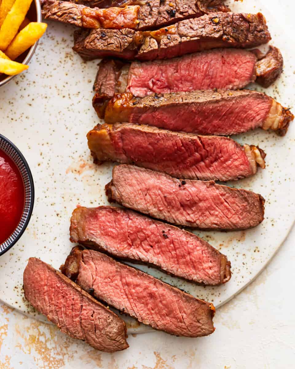 Steak with ketchup and fries on a white plate.