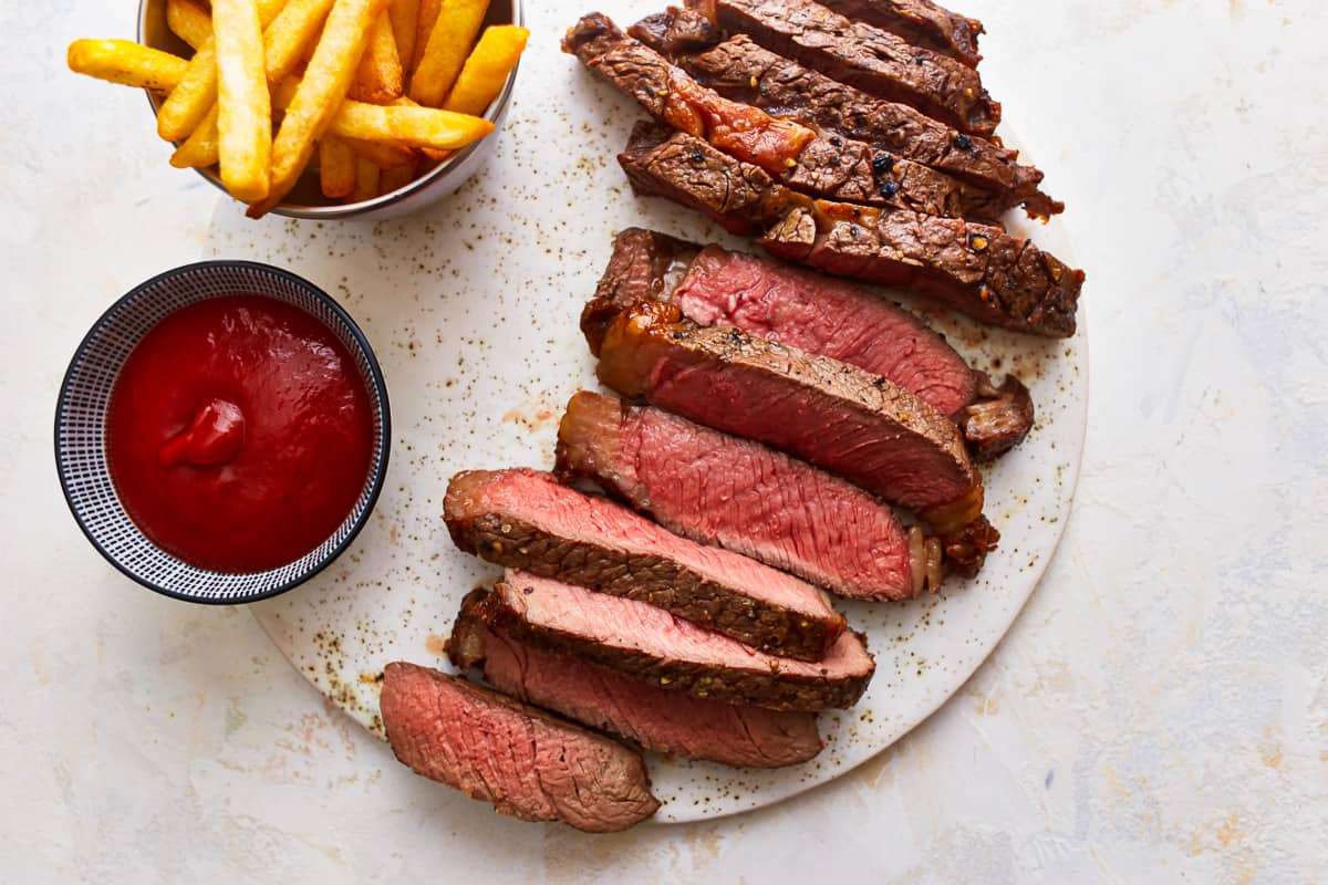 Steak dengan kentang goreng dan saus tomat di piring.