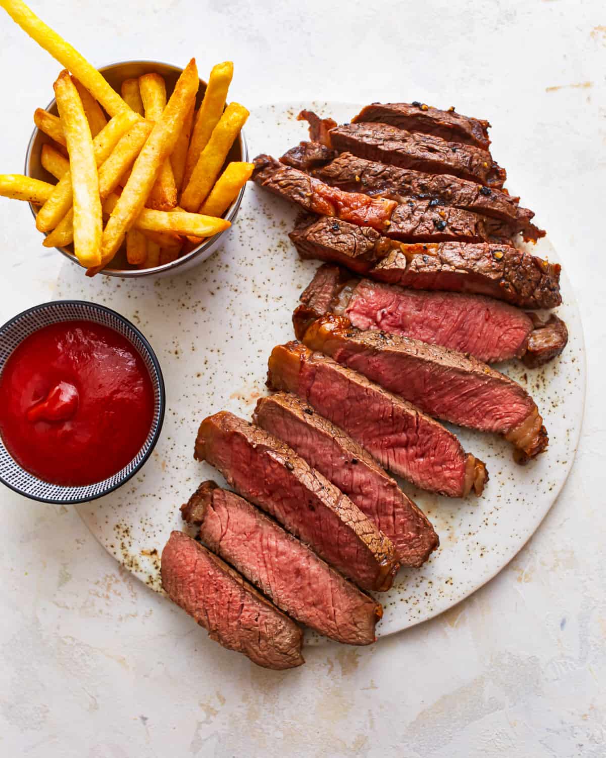 Air fryer ribeye with fries and ketchup on a plate.