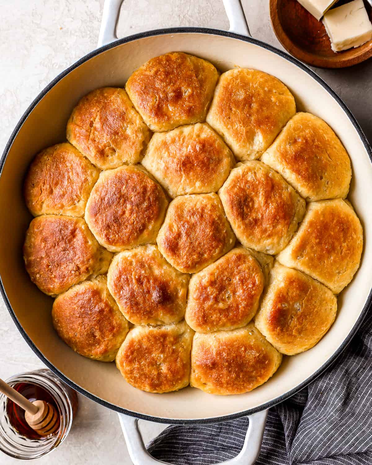 A skillet filled with angel biscuits, next to a jar of honey.