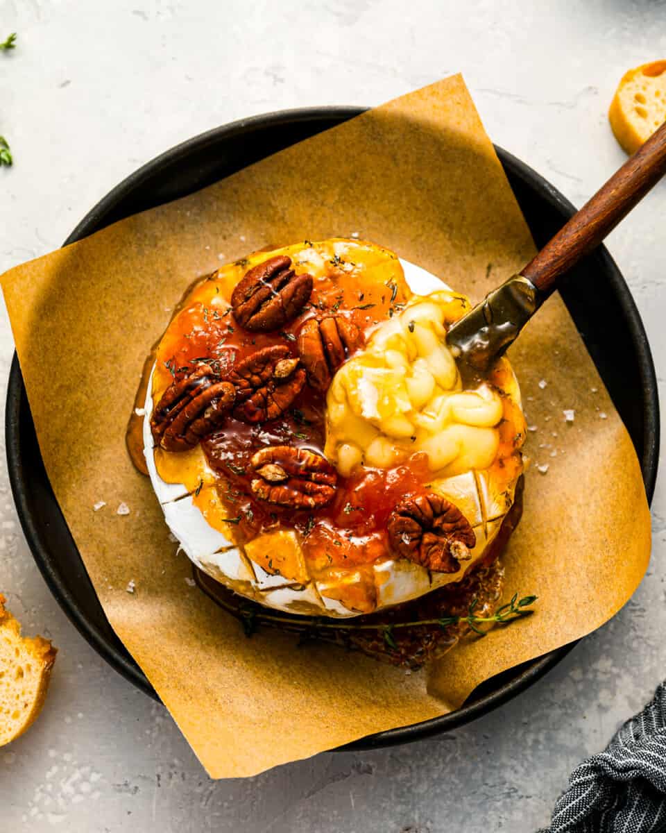 A plate of baked brie with jam and pecans on top.