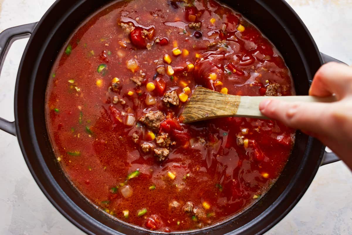 A person stirring a pot of Mexican beef soup with a wooden spoon.