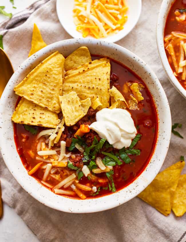 Two bowls of mexican chili soup with sour cream and tortilla chips.